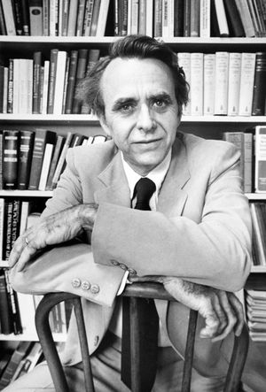 Black and white portrait of Professor Granville sitting in a suit with his arms crossed on a wood-backed chair in front of a shelf of books