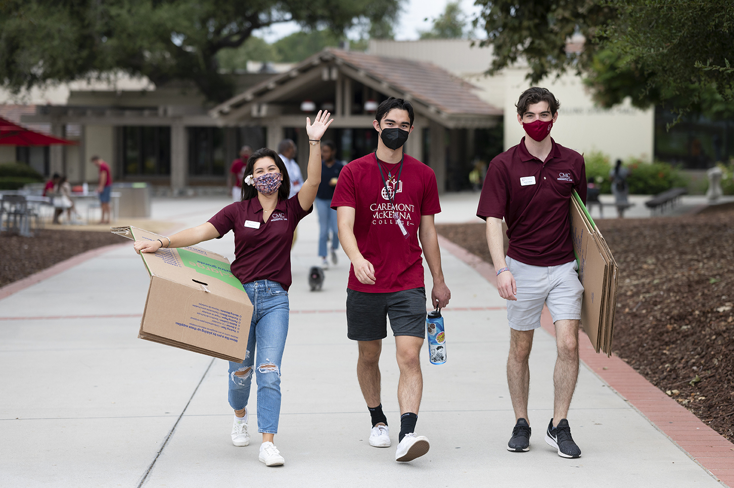 Three masked student walk down campus pathway with folded boxes in arms, ready to help students and families.