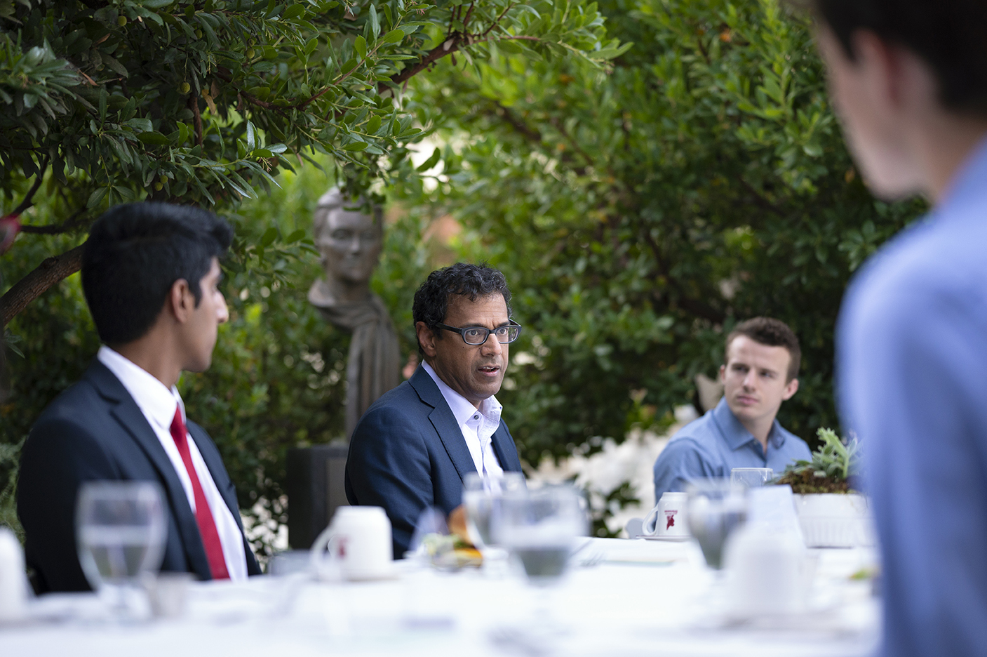 Dr. Atul Gawande sits at the outdoor Ath dinner head table with students surrounding him in conversation.