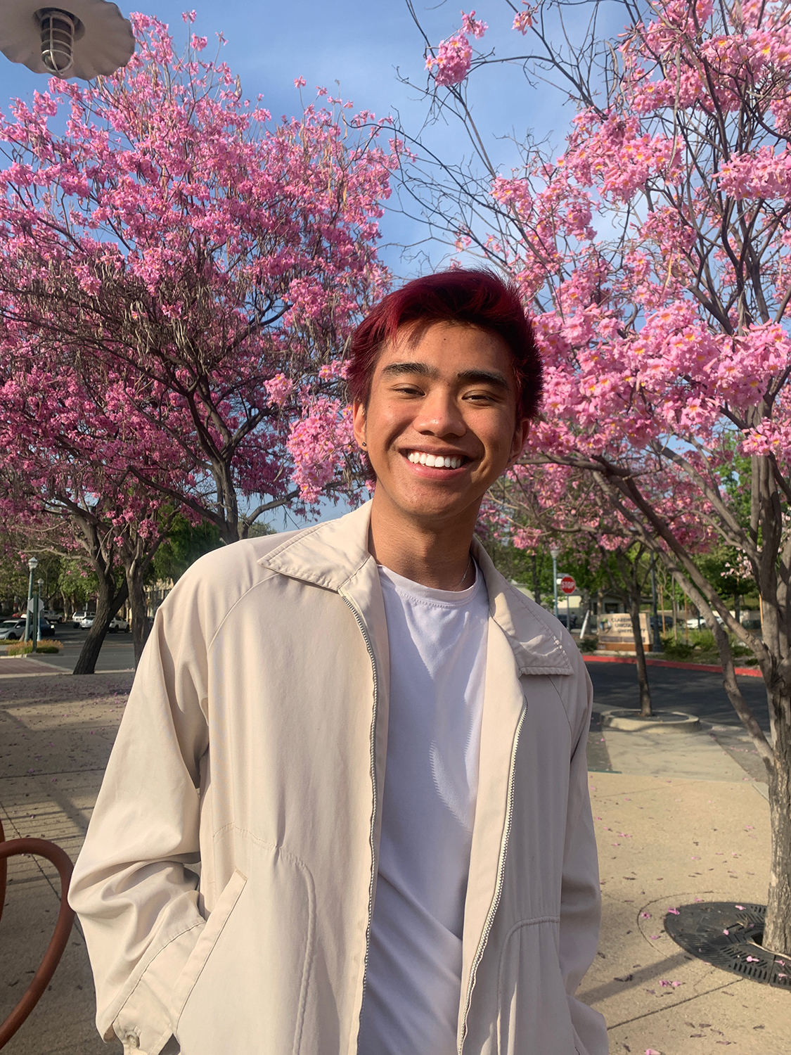 Jon Joey '23 stands smiling in front of blooming cherry blossom trees