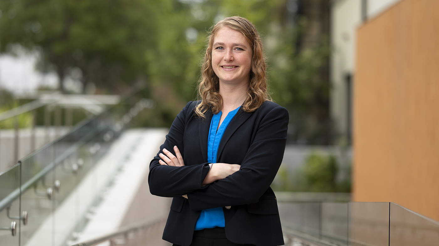 Professor Sarah Cannon poses with a smile and crossed arms on the glass ramp outside of Kravis Center.