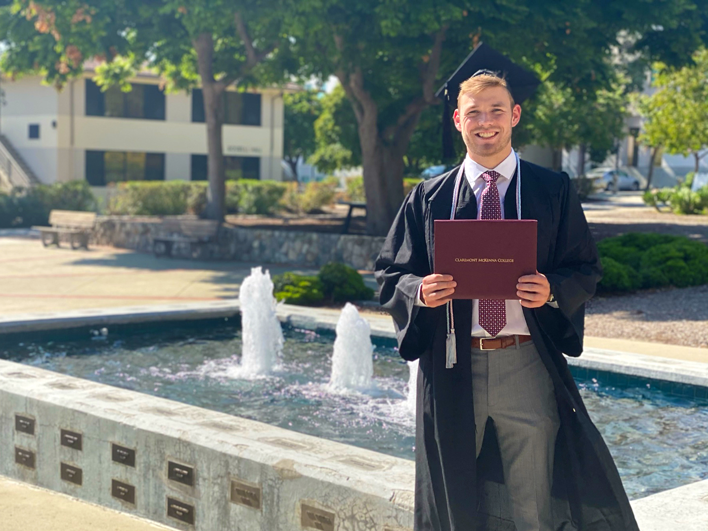 Hank Snowdon ’21 holds up his CMC diploma in cap and gown on campus