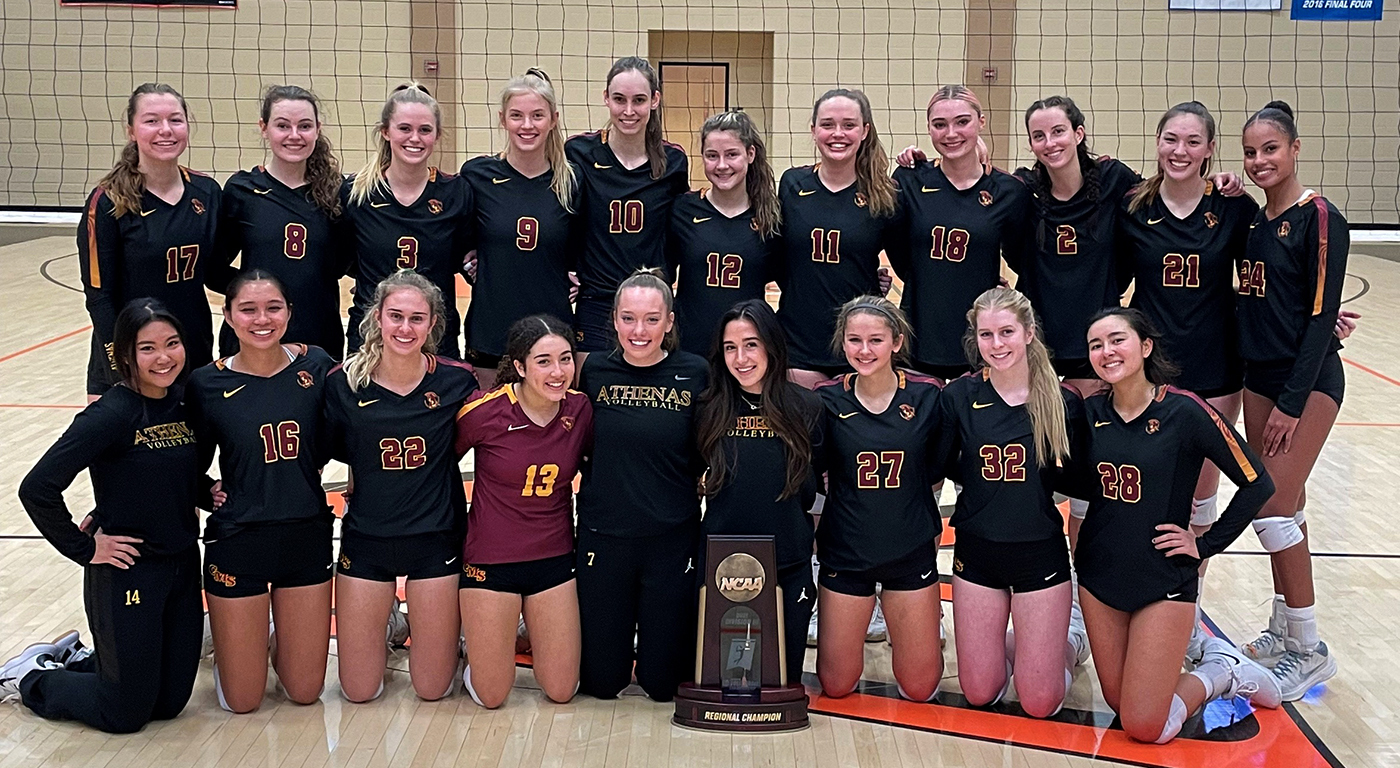 CMS Athenas Volleyball Team line up in two rows in front of a net for a group photo with their NCAA Regional Championship trophy.
