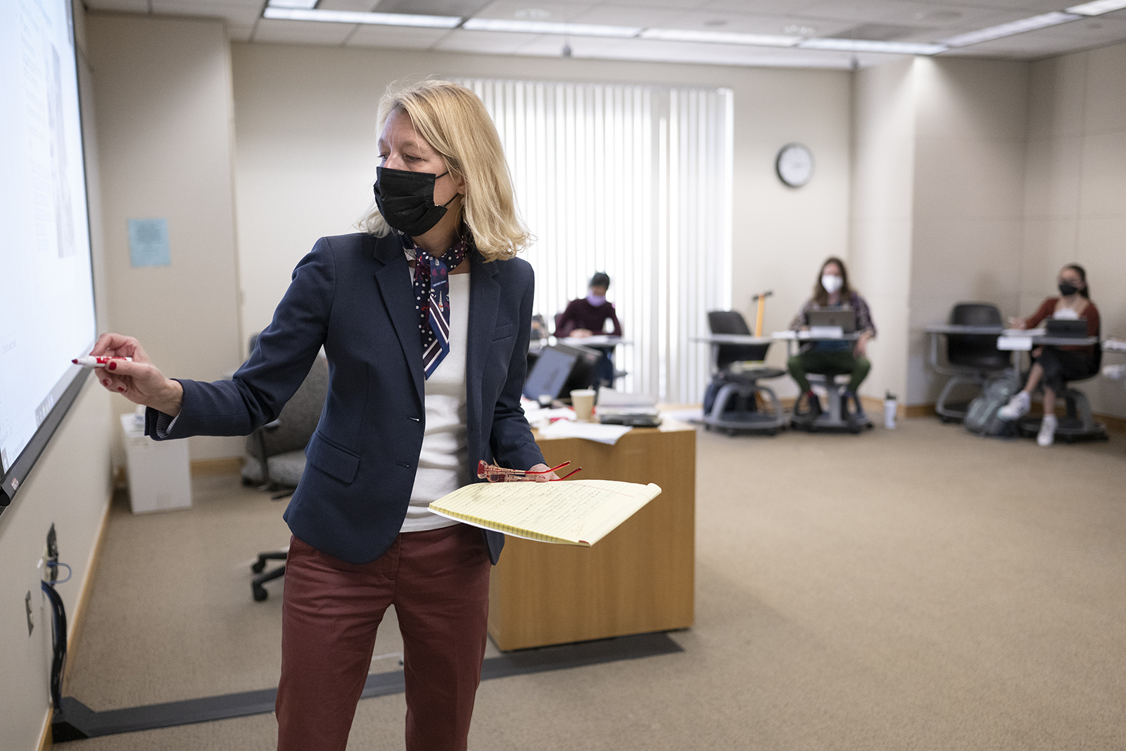 Candid photo of Professor Wendy Lower lecturing in front of a marker board and projector while a ring of students sit behind her.
