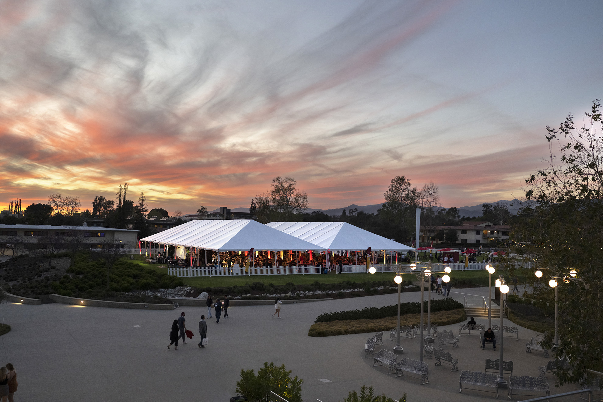 The sunsets displays vivid oranges, pinks, and yellows behind white event tents full of CMC community members.