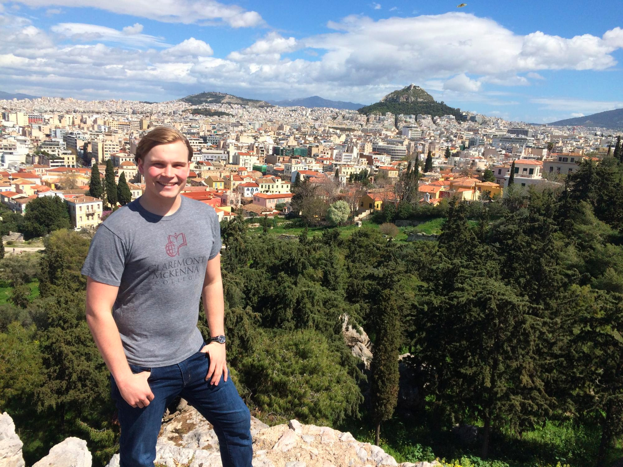 Portrait of Lucas Radice ’19 in a gray CMC t-shirt with a sunny city scape behind him.