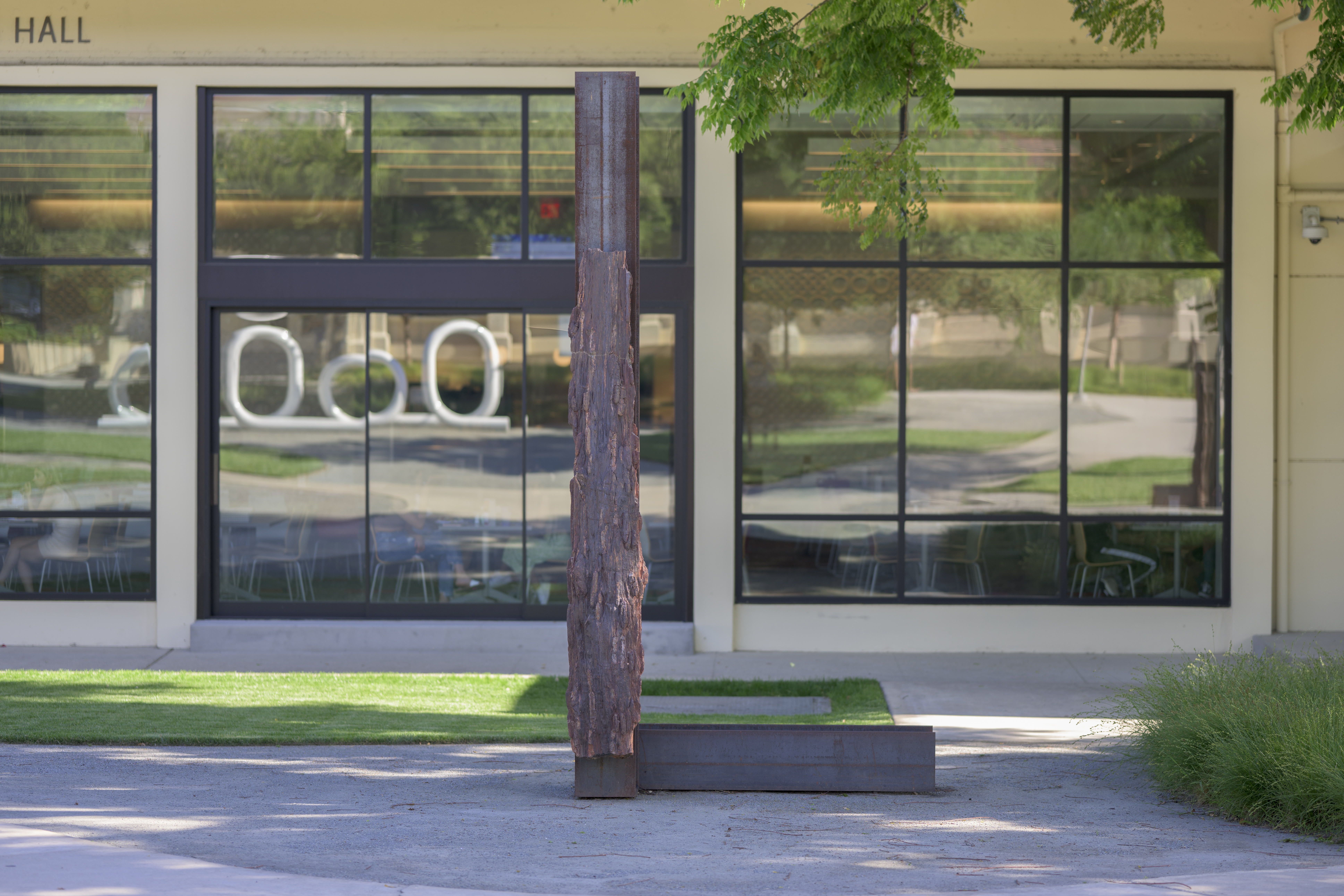 Photo of Carol Bove's Cretaceous on campus. In the background are the windows of Collin's Dining Hall reflecting Four Loops, another Bove piece, and students around campus.