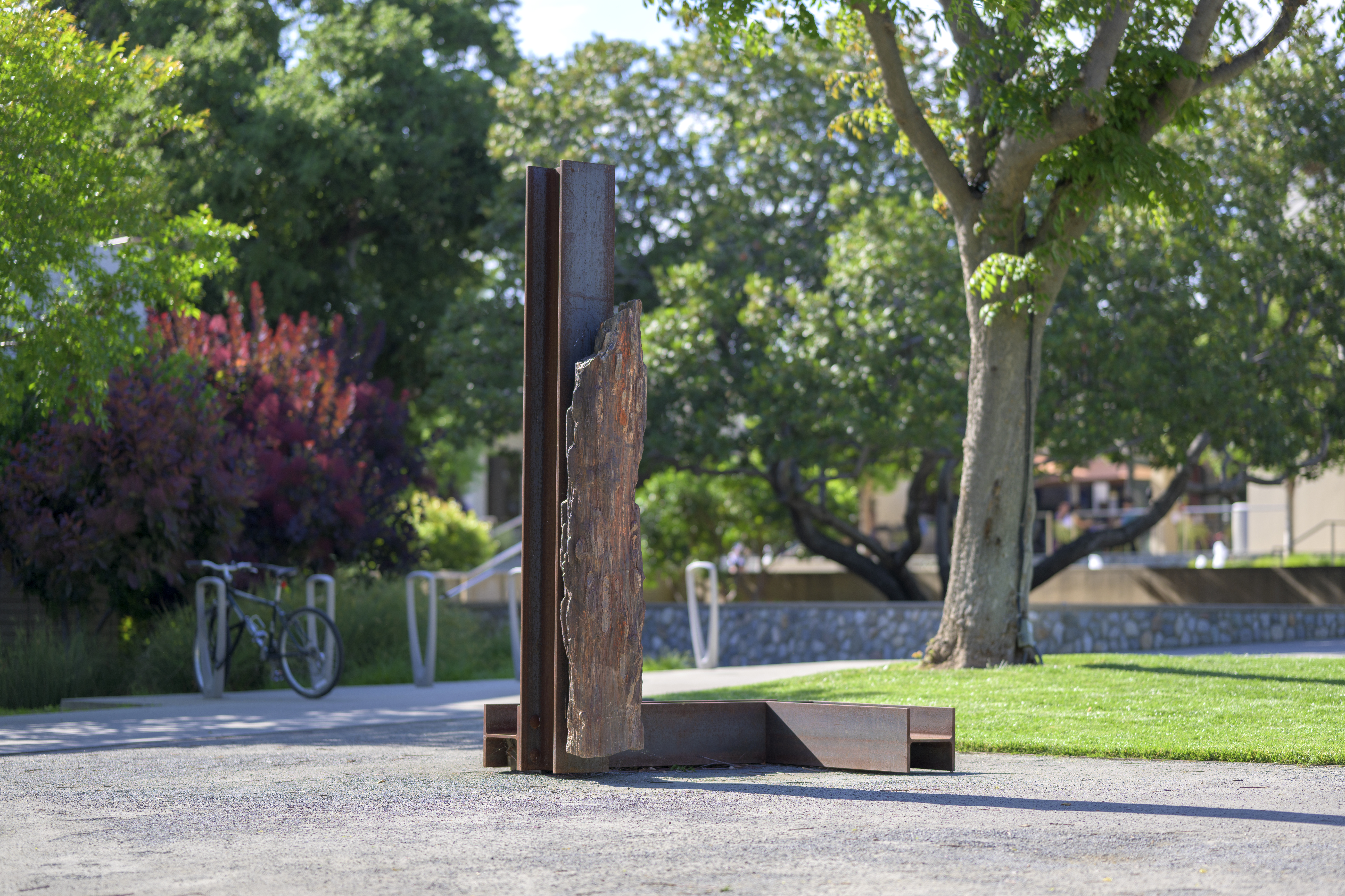 Photo of Carol Bove's Lingam on campus. In the background is a parked bicycle, trees, and students at the Hub.