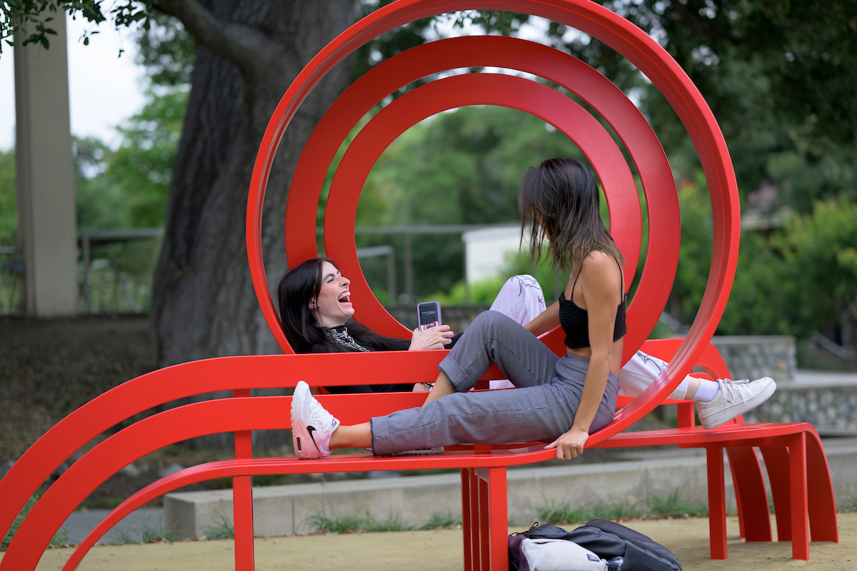 Two students sit on both sides of a looped bench.