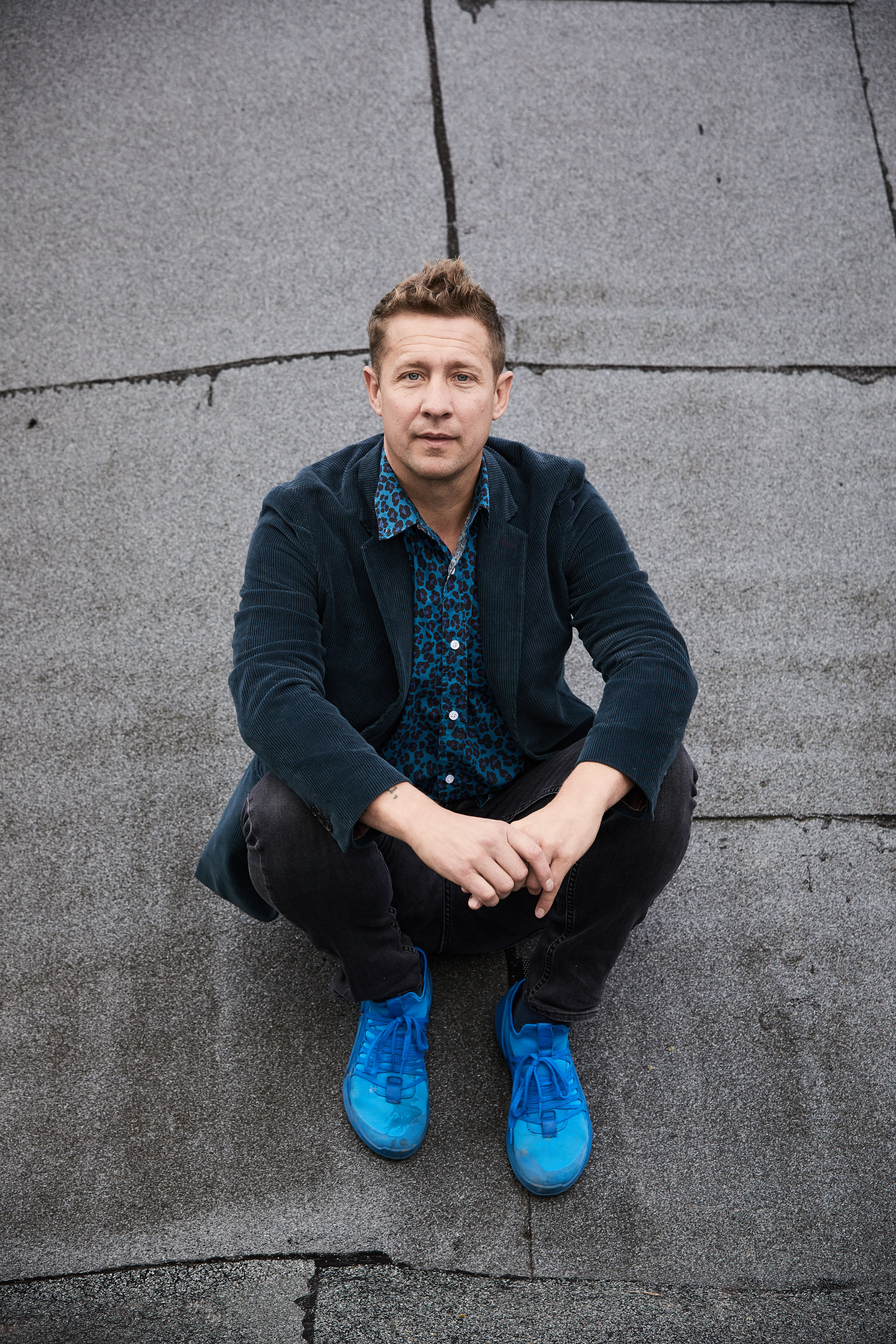 Artist Jeppe Hein seated on pavement wearing signature blue colors.