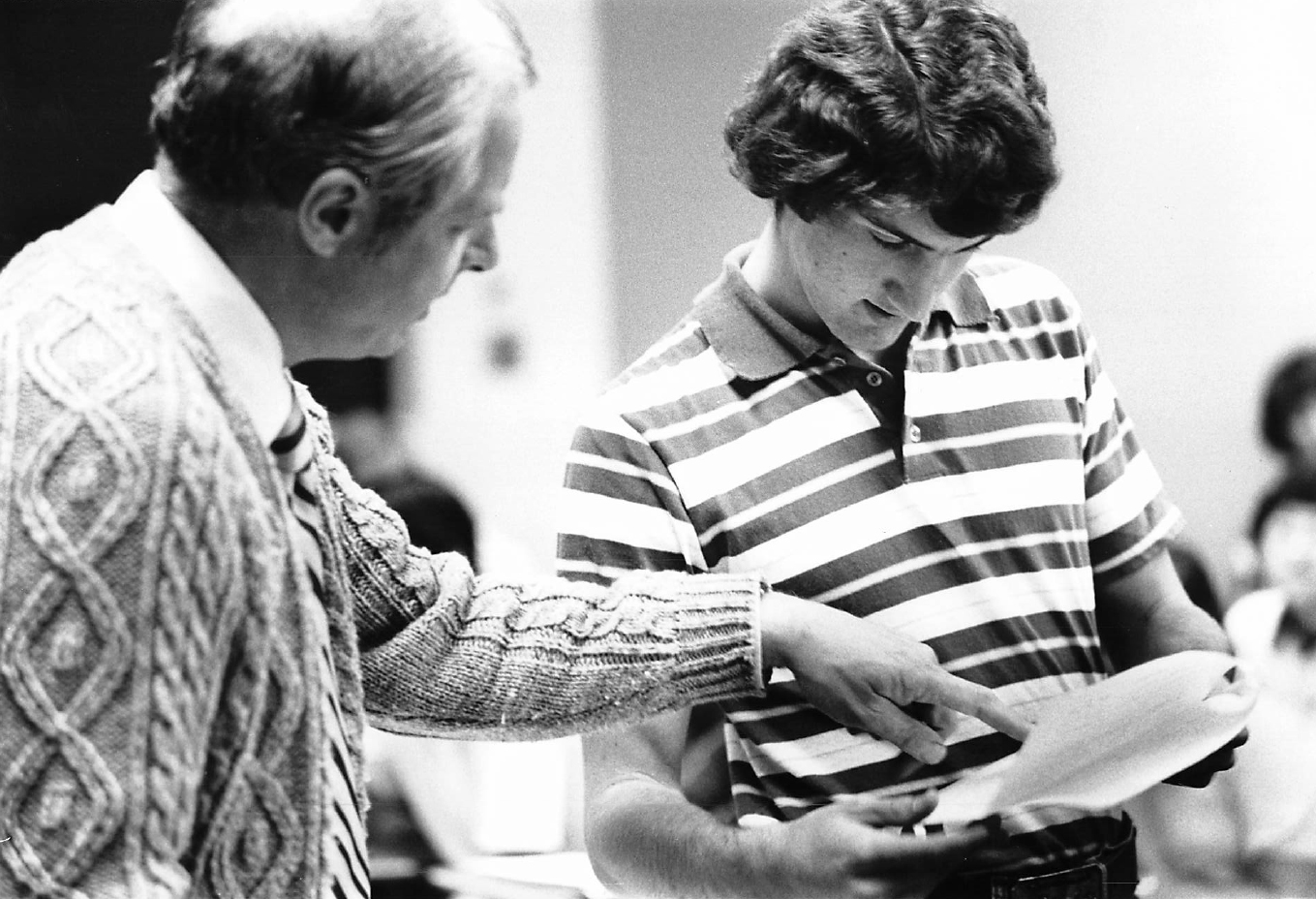 In a black and white candid photo, Professor John Ferling (left), remarks on a student's paper work (right) in class.