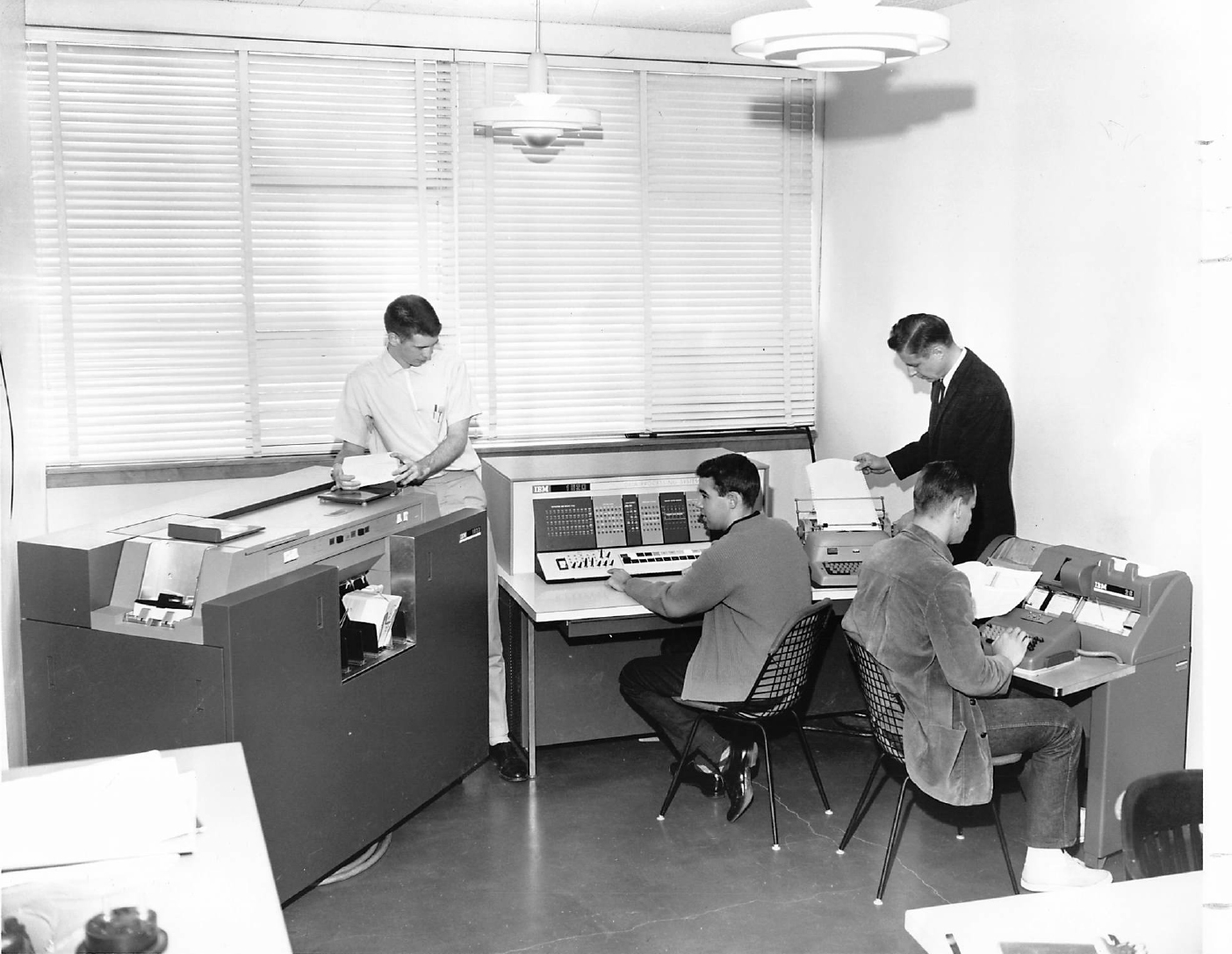 In a black and white photo, four students work on various (now vintage) computation machines.