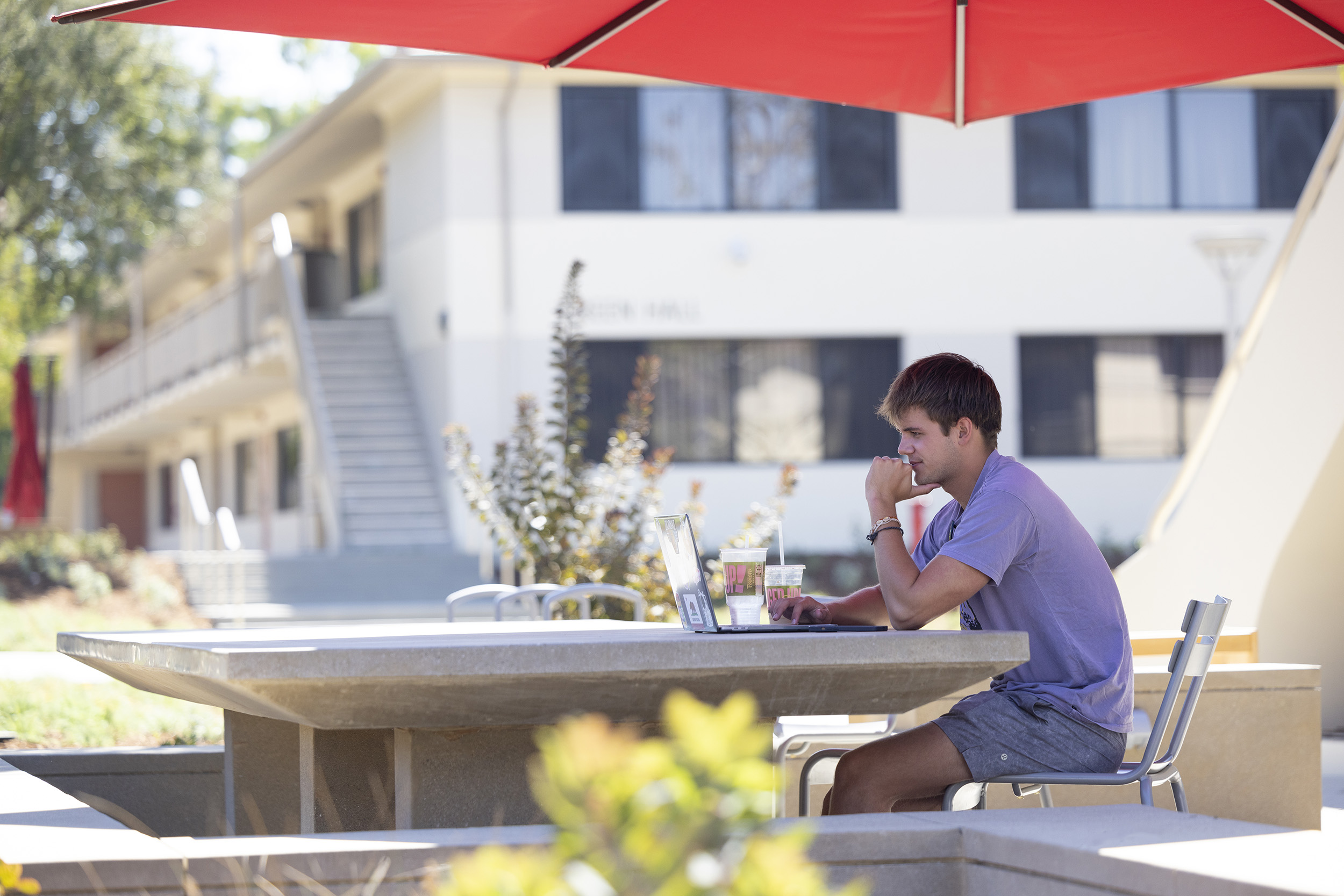 A student utilizes one of the shaded outdoor tables newly installed on campus.