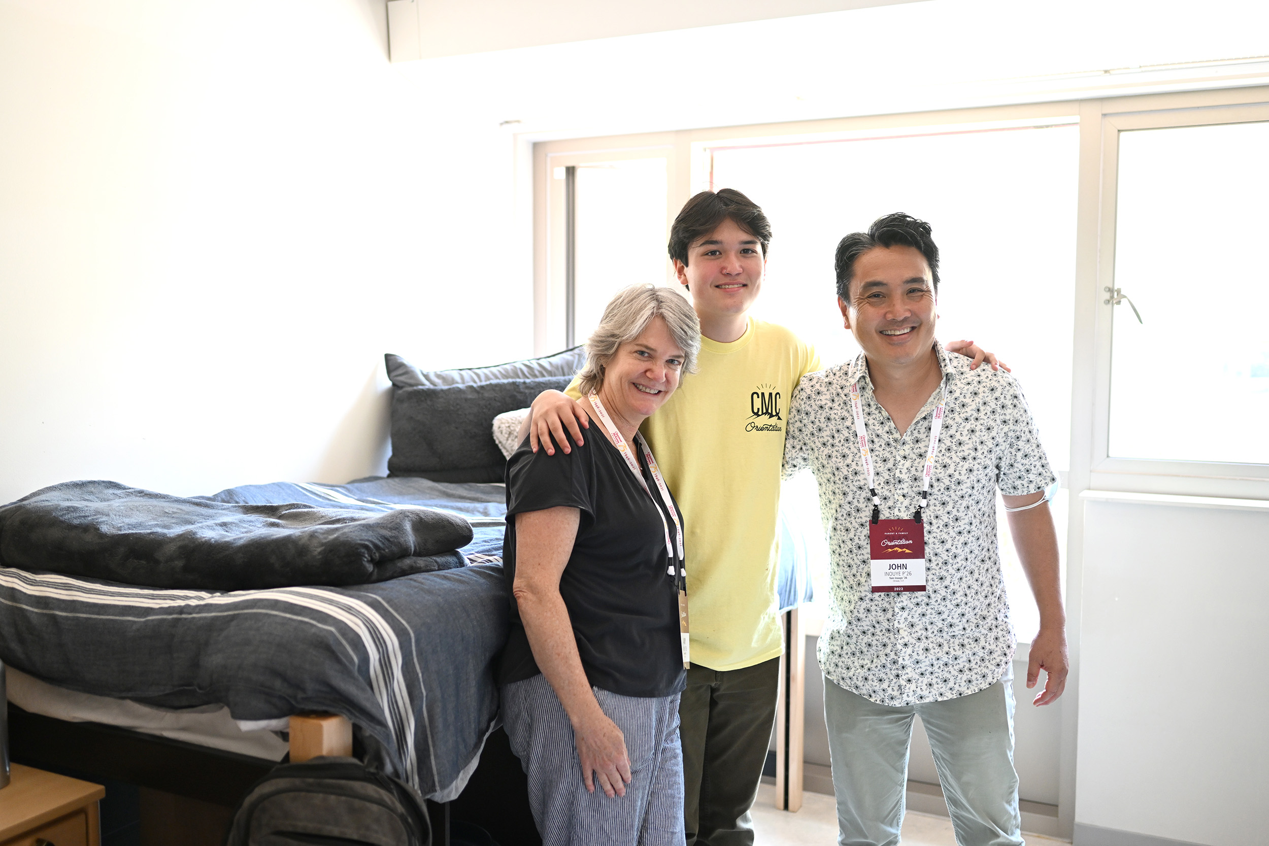 Tom Inouye ’26 stands before his freshly made bed with his arms around his parents.