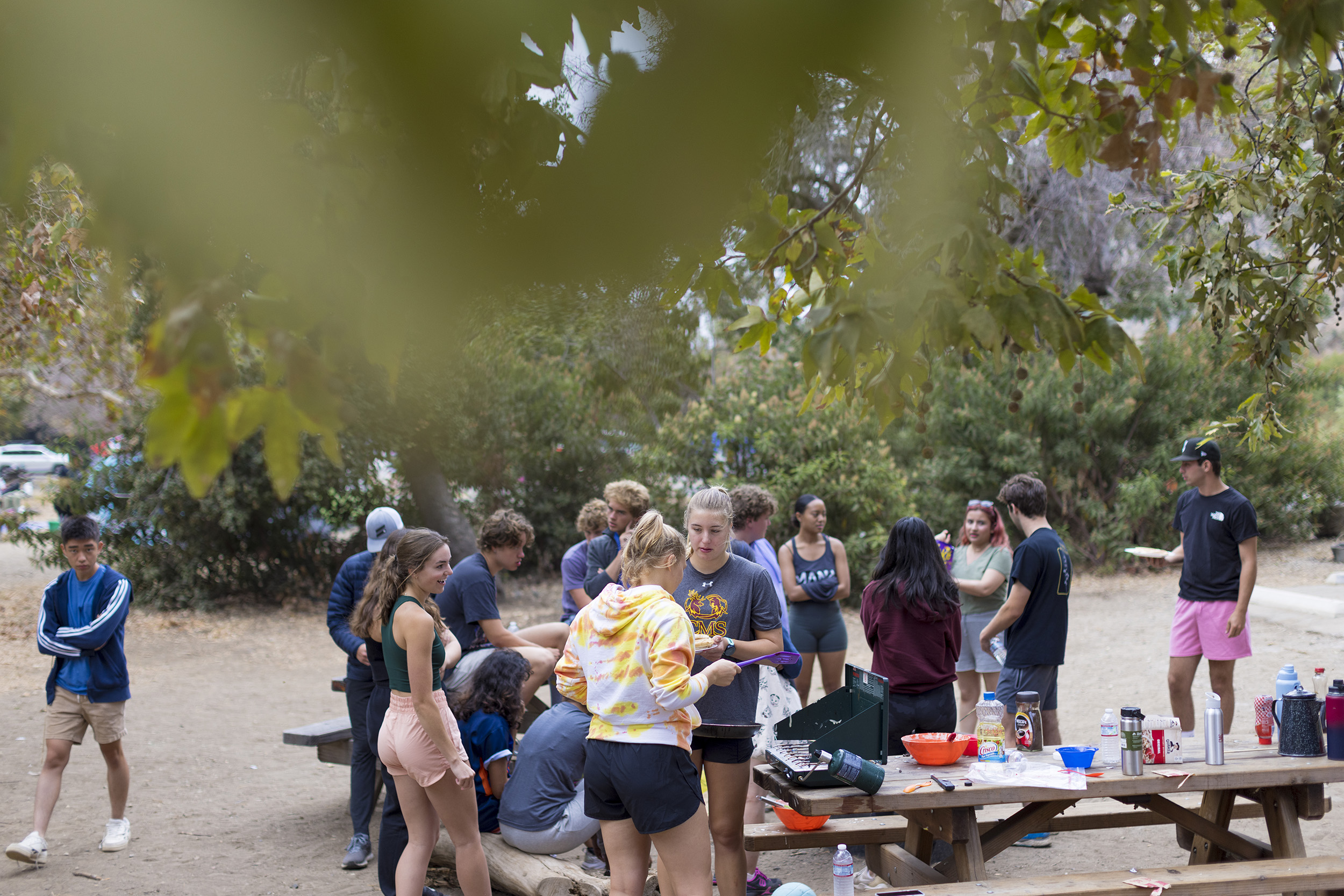 Students mingle around picnic tables set up with a portable grill and breakfast items.