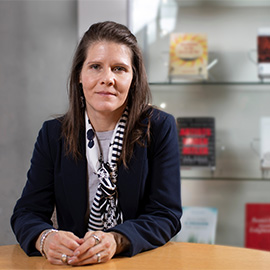 Professor Ferguson at a desk with a curated glass bookshelf behind her.