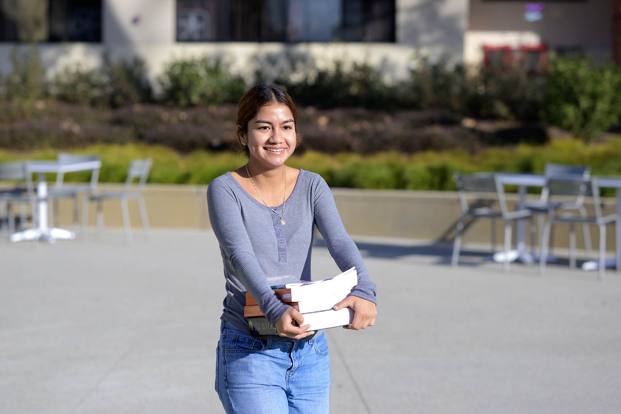 Female student carrying books across campus.
