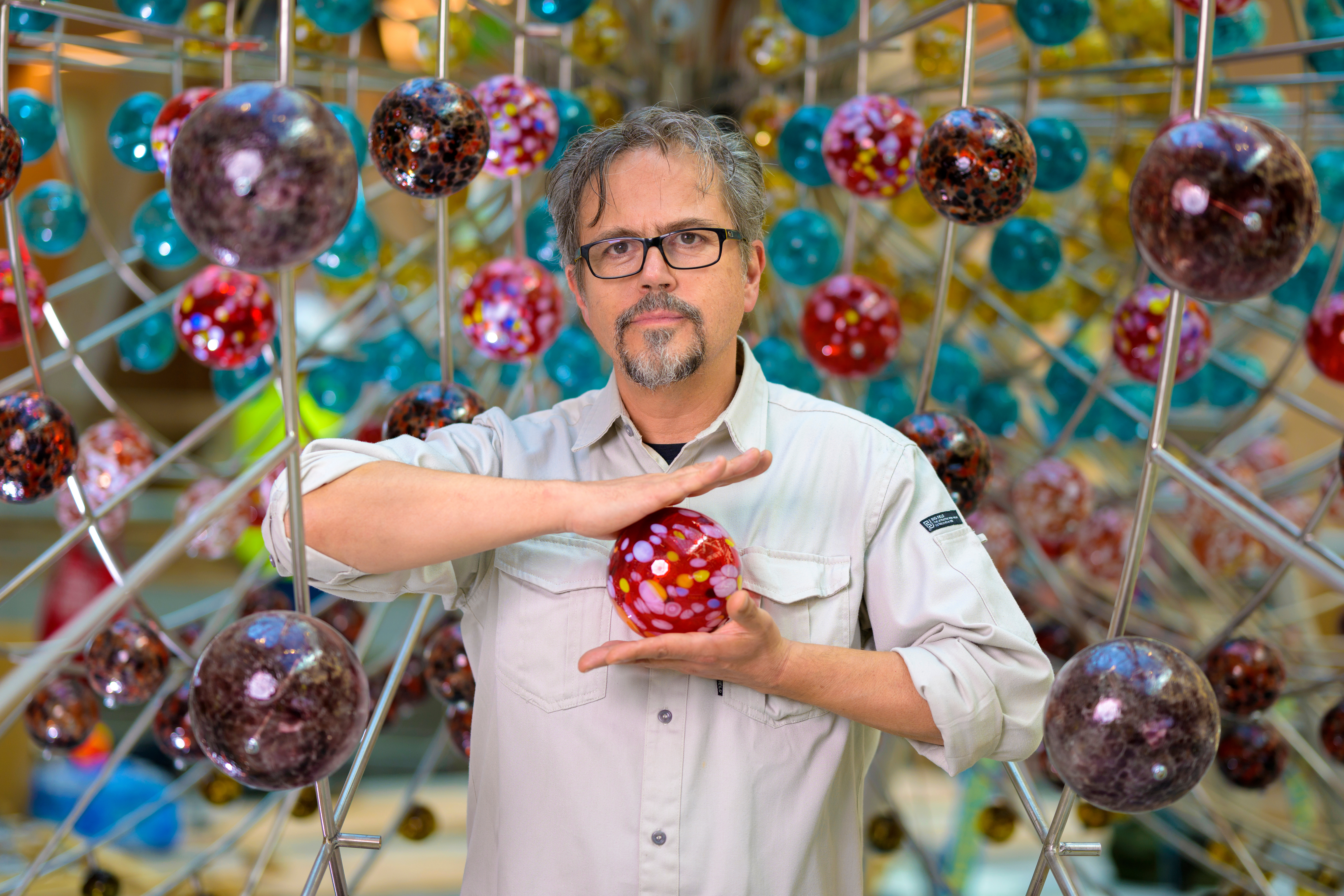 Damián Ortega, holding a red glass sphere, in front of his installation.