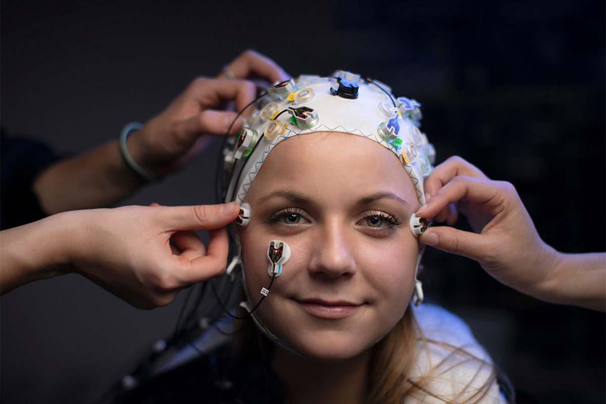 A female student with neurological scan equipment being attached to her head.