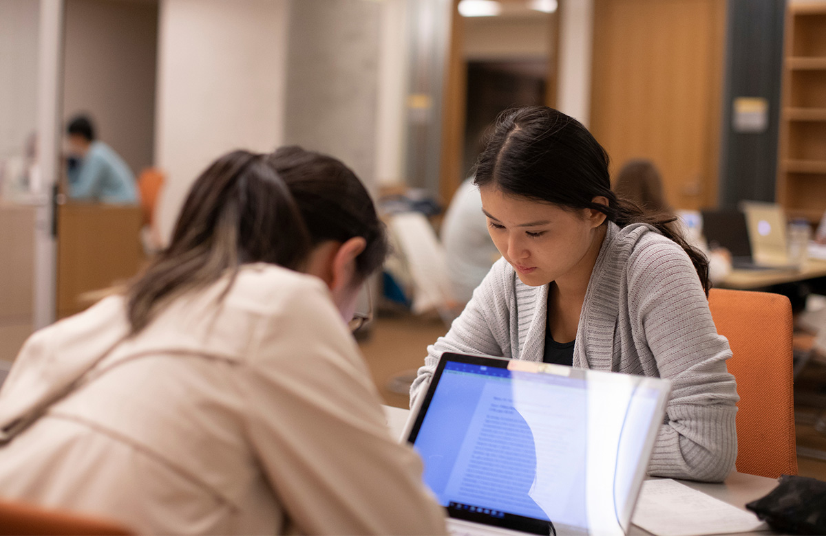 Two female students working on their laptops across from each other.