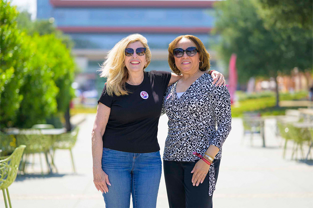 Mari Adam ’80 (left) and Lorraine Bains ’88 standing together on the North Mall.