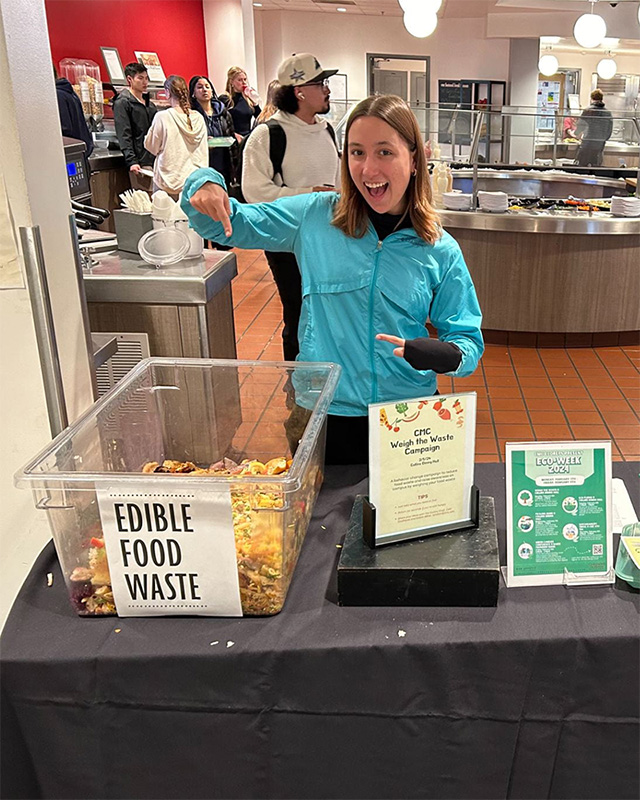 A student standing near the container collecting edible waste for a Weigh the Waste campaign.