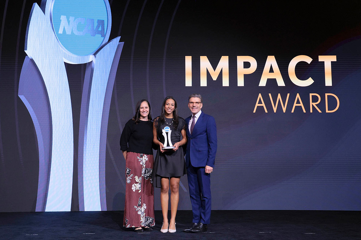 Ella Brissett ’25 on stage accepting her 2026 NCAA Impact Award. She is accompanied by Erica Jasper (left) and President Hiram Chodosh.