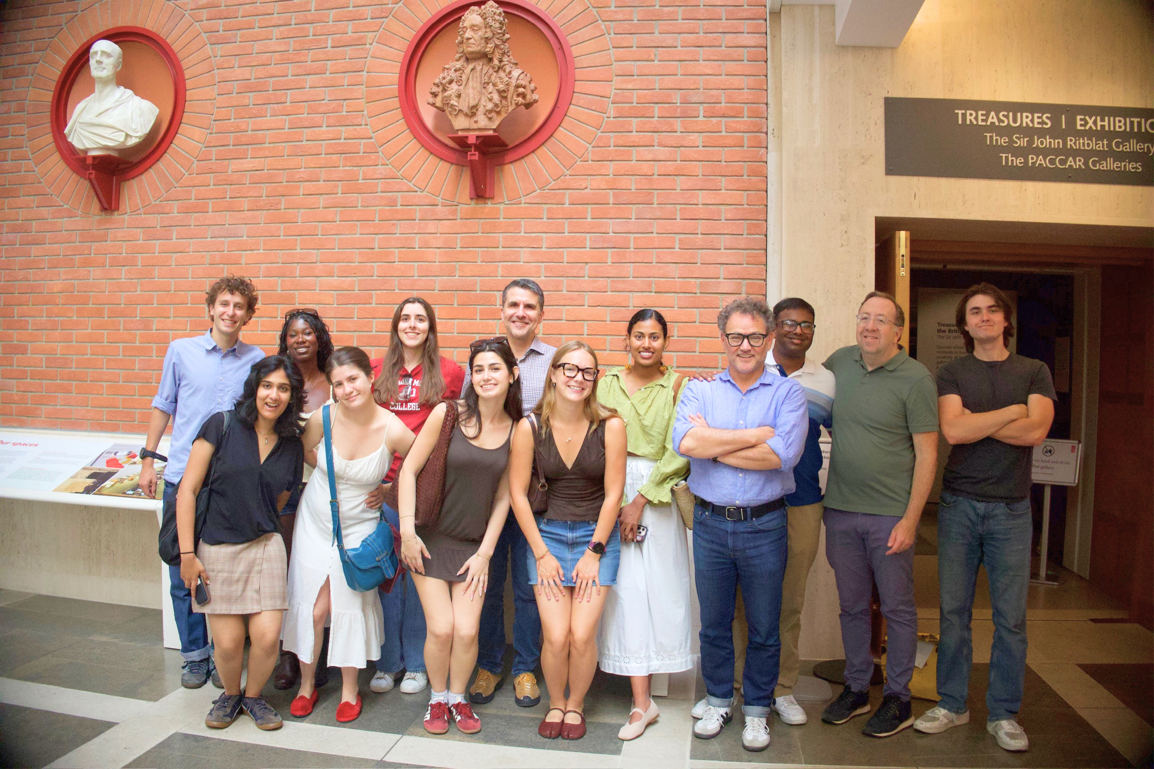 Group of male and female students, faculty, and staff posing in front of brick wall of The Paccar Galleries.