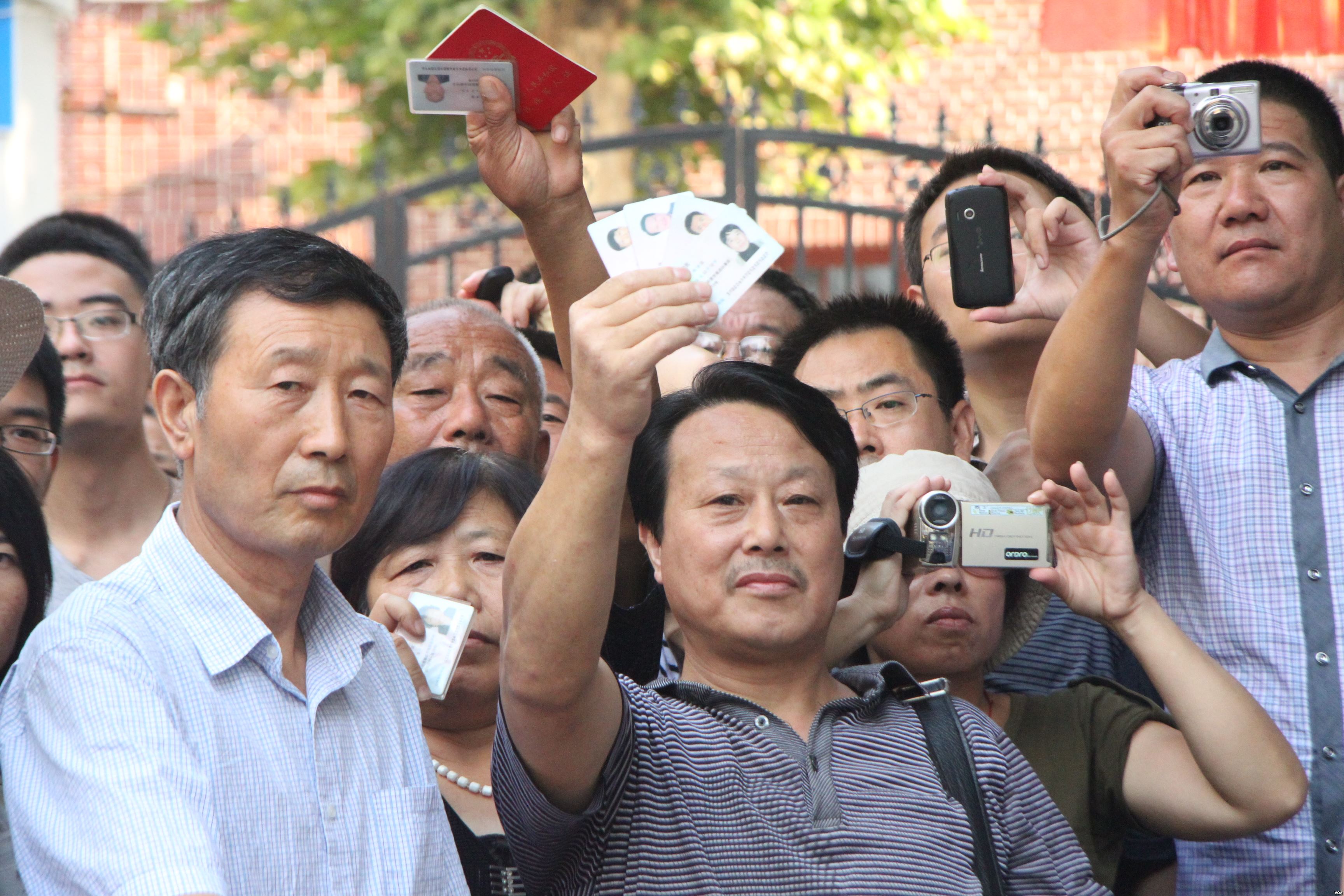 Chinese citizens holding up IDs and cameras at Bo Xilai trial