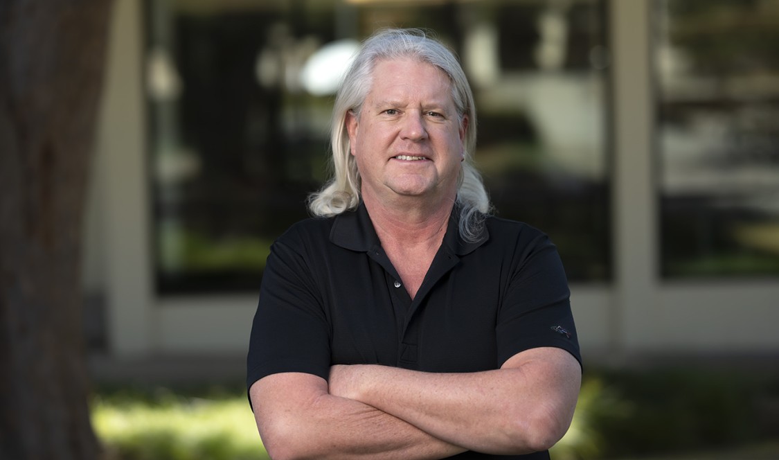 Professor Scot Gould poses on campus with his hair reaching past his shoulders from his pandemic experiment.