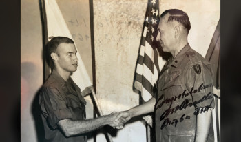 A signed black and white photo of Philip Chrones '66 in uniform shakes hands with a military senior.