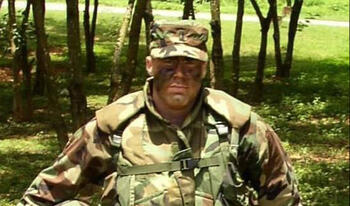 Man wearing military uniform standing outside in open grass field.