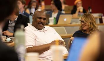 Man wearing white collar shirt sitting conversing with students.
