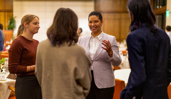 Woman in grey suit talking to two students after speaker series.