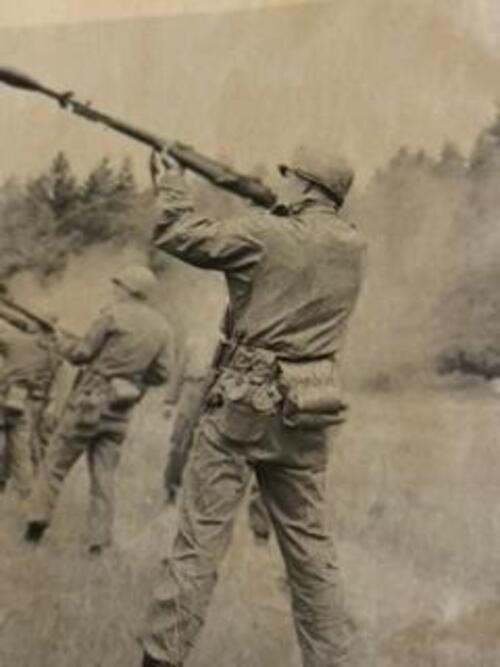 Man in military uniform holding rifle and shooting it into air.
