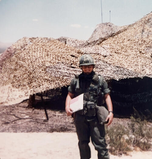 Man in military uniform standing in front of dunes holding a checklist.