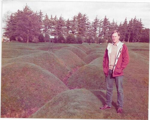 Man standing on grassy hills wearing red sweater and blue jeans. 