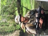 Man in military uniform holding rifle walking in swamp in forest. 