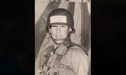 Man in khaki military clothing and gear with hard hat on.