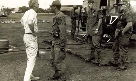 Men on military base in uniform in front of helicopter talking.