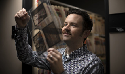 CMC Archivist Sean Stanley holding up photos from the school archive
