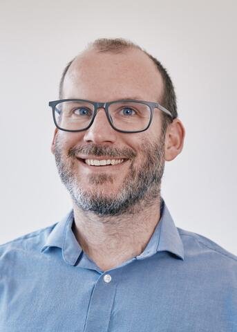 Man smiling wearing a blue shirt and glasses.