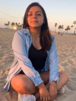 Photo of Karen Almachi at a beach with the sunset and palm trees behind her.