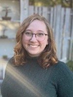 Smiling woman with glasses wearing green turtleneck shirt.